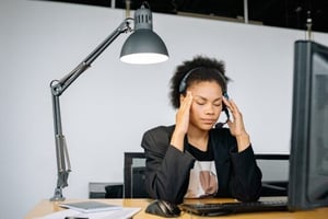A stressed employee sitting at their desk with their head in their hands, surrounded by paperwork and a laptop, symbolising the emotional and physical toll of burnout.