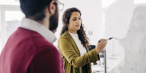 A woman wrtiting on a whiteboard whilst a colleague watches